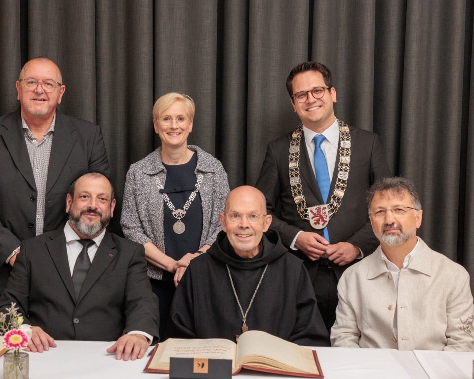 Imam Mustafa Cimsit, rabbijn Aaron Malinsky en Dom Adriaan Lenglet ontvangen de Martin Buber-Plaquette zitten aan tafel. Achter hen staan burgemeester van Kerkrade Petra Dassen, de burgemeester van Herzogenrath Benjamin Fadavian en een andere man.